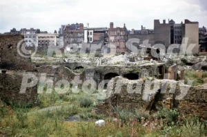 A 1950s colour photo of the extensive bomb damage and ruins in the Cripplegate area of London, featuring derelict brick foundations and wildflowers growing amongst the rubble.