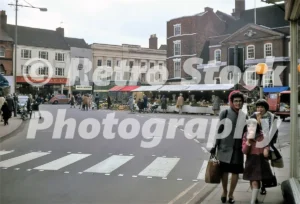A 1972 color photograph of the High Street and Market Place in Louth, Lincolnshire, featuring a zebra crossing in the foreground, local shops like F.W. Woolworth & Co Ltd, and people eating ice cream.