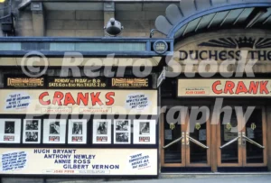 A 1950s colour photo of the front of the Duchess Theatre in London, displaying large promotional boards for the revue Cranks featuring cast members Anthony Newley and Annie Ross.