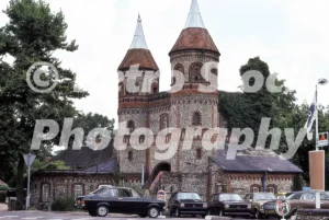 The flint and brick towers of Horsley Towers in East Horsley during the 1970s with Ford Escort and Fiesta cars in the foreground.