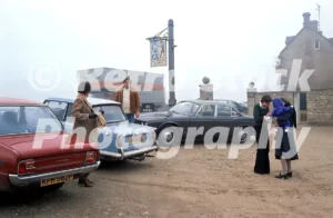 The car park of the Inn For All Seasons near Burford in the 1970s featuring a red Mazda and a light blue Triumph Herald under a foggy sky.