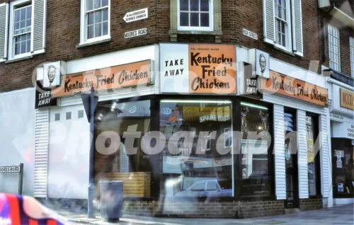 A Kentucky Fried Chicken takeaway on the corner of High Street and Moores Road in Dorking during the 1970s with vintage orange signage.