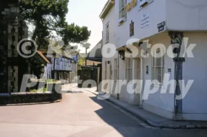 A sunlit view of the white-walled Kings Arms inn on Church Street in Sandwich during the 1970s, with St Mary’s Church visible to the left.
