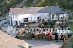 A 1975 photograph of the Lulworth Marine building at Lulworth Cove, Dorset, featuring lobster pots, fishing equipment, and holidaymakers in 1970s attire.