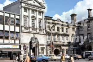 A 1970s street scene in Stafford Market Square featuring the National Westminster Bank, Stantons the Bakers, and period cars including a blue Ford Cortina.