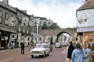 A 1970s photograph of Marygate in Berwick-upon-Tweed, featuring a policeman directing traffic through the historic Scotsgate arch and various period vehicles, including a white Austin with the registration RTY 292.