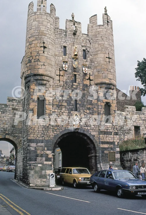 1980s photo of Micklegate Bar in York with a blue Lancia Gamma Berlina and a mustard Volvo 245 estate passing through the gate.