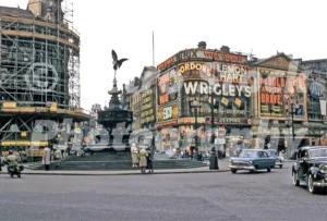 A 1950s colour photo of Piccadilly Circus in London, featuring the statue of Eros and the Monico building on the left with its famous neon advertisements removed and replaced by scaffolding.