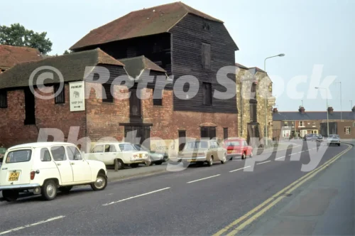 A 1970s photograph of a street in Rye, East Sussex, featuring historic red-brick and black timber-clad warehouses, a sign for the Ship Inn, and period cars including a white Renault 4