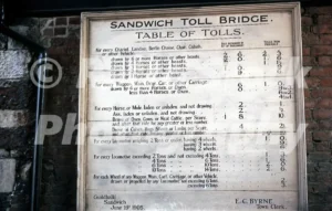 A 1971 photograph of a historic wooden "Table of Tolls" sign for the Sandwich Toll Bridge in Kent, mounted on a brick wall and dated June 19th 1905.