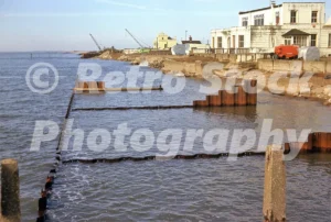 A 1970s photograph of coastal engineering at Felixstowe, Suffolk, showing new rusty steel sheet piling groynes being installed in the sea in front of the white-fronted Marlborough Hotel.