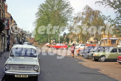 1980s photo of High Street, Moreton-in-Marsh with a white Bedford HA van, parked cars and trees beside the market area.