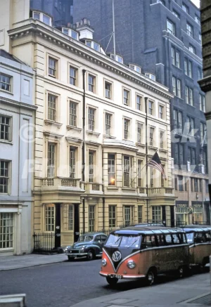 A 1950s colour photo of Douglas House on Brook Street, London, in 1958, featuring the American flag and three Volkswagen Type 2 minibuses.