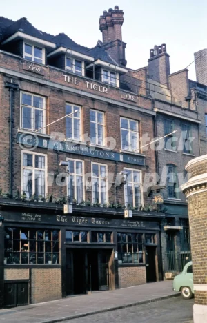 A 1950s colour photo of The Tiger Tavern at Tower Hill in London, showing its brick facade with "Charrington's Ales & Stout" signage and historical dates.