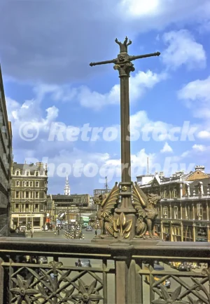 A 1950s colour photo of Holborn Viaduct in London, featuring an ornate bronze dragon boundary mark in the foreground and a view looking towards the steeple of St Bride's Church.