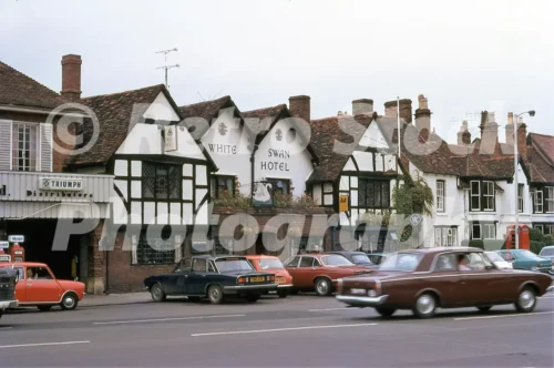 A 1971 photograph of the White Swan Hotel in Stratford-upon-Avon, featuring a historic timber-framed building with three gables, a Trust House sign, and a row of parked cars including a Triumph and an Austin.