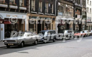 A 1960s colour photo of period cars parked outside elegant boutique shopfronts on Brook Street in Mayfair, London.