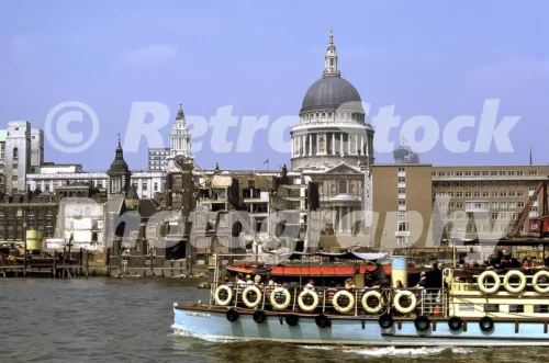 1960s photo of St Paul’s Cathedral seen from the River Thames, with riverside demolition sites, wharves and a passenger boat in the foreground.