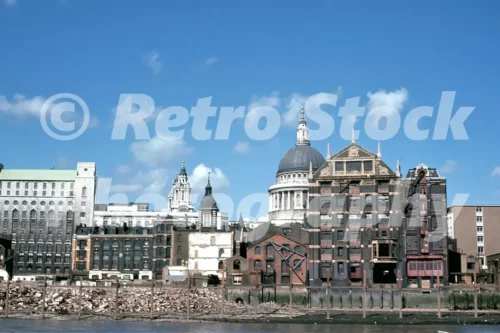A 1960s colour photo of the River Thames shoreline featuring the brick facade of Paul's Wharf warehouses with the dome of St Paul's Cathedral in the background in London in 1968.