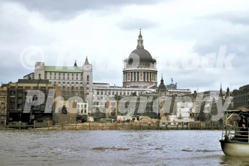 A 1960s colour photo of a pleasure boat on the River Thames with the dome of St Paul's Cathedral rising behind a series of partially demolished brick wharves in London in 1968.