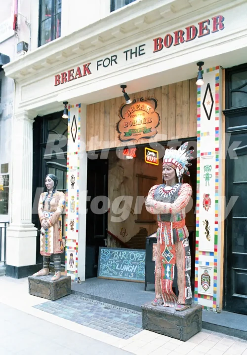 1980s photo of Break for the Border on Argyll Street, London, next to the London Palladium, with painted frontage, neon signs and large doorway figures outside.