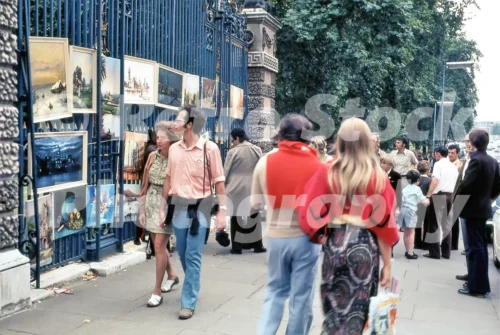 A 1970s colour photo of pedestrians browsing paintings at the Sunday art market on the Piccadilly railings of Green Park in 1972.