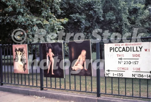 A 1970s colour photo of paintings for sale on the railings of Green Park along Piccadilly in 1972 with a City of Westminster street sign in view.