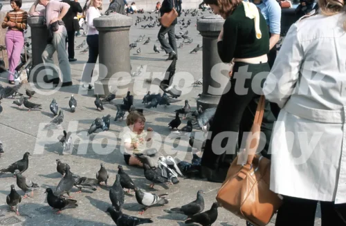 1970s photo of a small child crying among pigeons in Trafalgar Square while adults in flared trousers and 1970s clothes stand nearby