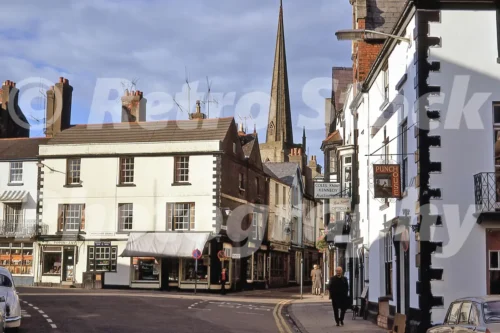 A 1972 photograph of Agincourt Square in Monmouth, looking toward the Shire Hall and the statue of Henry V, with period cars and a view of St Mary's Church spire in the distance.