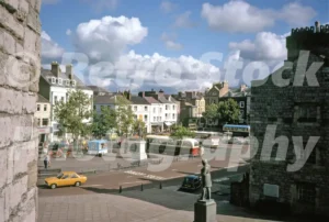 A 1975 elevated photograph of Castle Square in Caernarfon, featuring several single-decker buses, and statues of local figures overlooking the pedestrianised plaza.