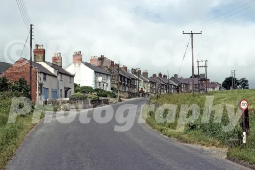 1960s view of a road through Coedpoeth near Wrexham in Wales with terraced houses, telegraph poles and open fields