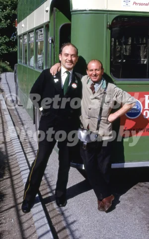 A 1969 photograph of a bus driver and conductor posing together in uniform beside their green double-decker bus on a sunny day in Wrexham.