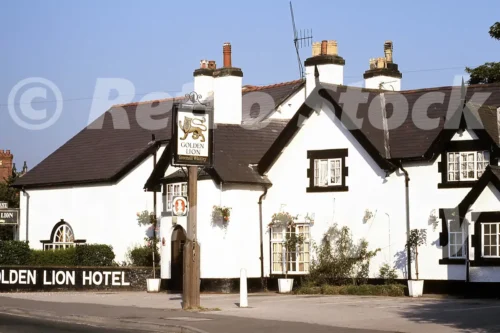 A 1970s view of the white Golden Lion Hotel in Rossett featuring black timber trim, a Greenall Whitley pub sign, and flower baskets.
