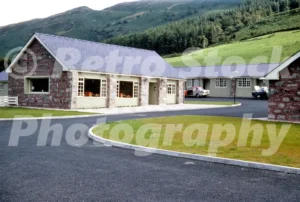 A 1960s photograph of the Snowdonia Park Motel near Bethesda, featuring the stone-built reception building and green guest wings with a white and red Sunbeam Rapier parked in the asphalt courtyard.