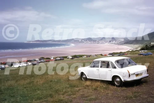 Austin 1800 at Putsborough Beach in Devon in the 1970s with Woolacombe in the distance, parked cars and wide sandy bay