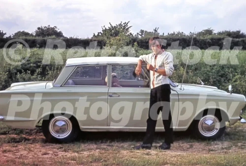 1960s photo of a Ford Cortina parked in the countryside with a young man leaning against the car