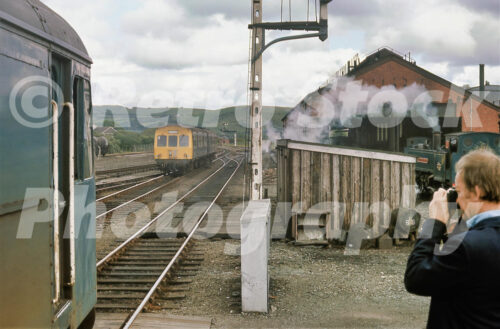 1970s view of Aberystwyth station in Wales with a British Rail diesel multiple unit approaching and a Vale of Rheidol steam locomotive beside the engine shed