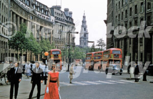 A 1950s colour photo of the sweeping curve of Aldwych with red double-decker buses and a woman in a red polka dot dress in 1957.