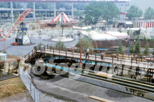 A 1960s color photo of the log flume ride at the New York World's Fair amusement area, featuring guests in a log boat, a wooden pedestrian bridge, and an Orange Julius stand in the background.