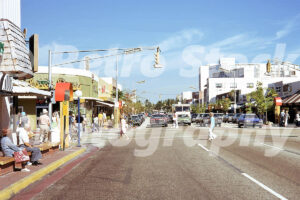 A 1970s color photo of 95th Street in Surfside, Florida, showing people waiting at a bus stop, shops like Sunny's, and vintage cars including a blue AMC Gremlin and a brown Cadillac.