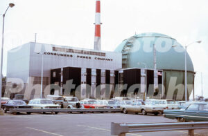 A 1960s color photo of the Big Rock Point Nuclear Power Plant in Michigan, featuring the iconic green containment sphere, the Consumers Power Company building, and a parking lot filled with vintage cars.