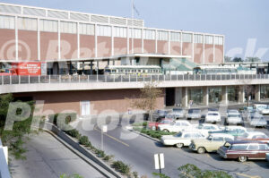 A 1960s color photo of the bus terminal and parking lot at Northland Center in Southfield, Michigan, featuring vintage Detroit city buses, a Speedway Messenger truck, and the Hudson’s building.