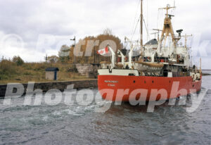 A 1970s colour photo of the CCGS Montmorency, a red Canadian Coast Guard ship from Ottawa, navigating the Sault Ste. Marie Canal with autumn trees in the background.