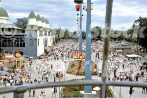 A 1960s color photo of the Cedar Point midway in Sandusky, Ohio, featuring the Sky Ride gondolas overhead, a crowded pedestrian walkway, and the Coliseum building on the left.