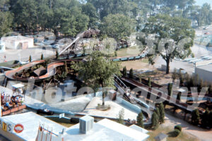 A 1970s color photo of the Mill Race log flume at Cedar Point in Sandusky, Ohio, featuring several log boats navigating a winding watercourse through trees, with the park museum and midway visible in the background.