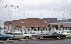 A 1960s color photo of the Dayton's department store at Southdale Center in Edina, Minnesota, featuring a textured brown facade with script signage and a parking lot filled with vintage cars.