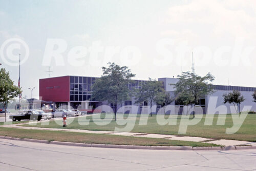 A 1960s color photo of the modernist Dearborn Police station with a red accent wall and vintage patrol cars in 1967.