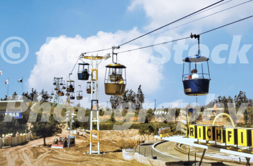A 1950s color photo of the Skyway buckets passing over Holiday Hill at Disneyland in California, with the Richfield Autopia signage and track visible in the foreground.