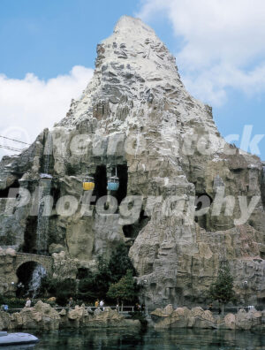 A 1960s color photo of the Matterhorn Bobsleds mountain at Disneyland in California, featuring Skyway buckets passing through the cavernous peak above a waterfall and the Submarine Voyage lagoon.