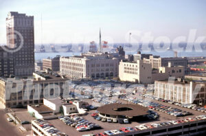 A 1970s color photo of the Detroit News Building with its neon rooftop sign and the red-brick Fort Shelby Hotel overlooking downtown parking lots in 1970.